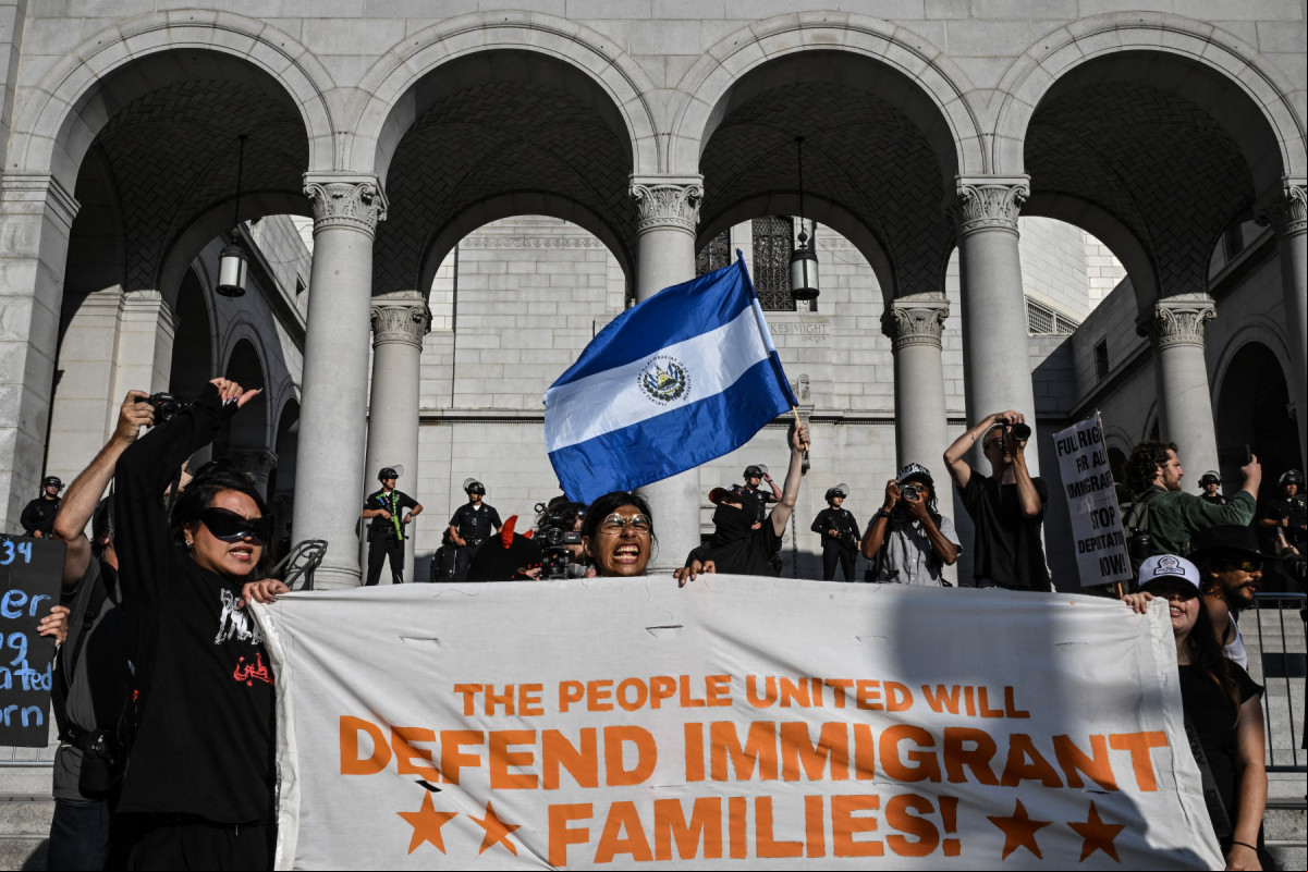 Um manifestante agita uma bandeira salvadorenha enquanto pessoas protestam em frente à Prefeitura de Los Angeles contra as operações federais de imigração em 11 de junho de 2025. Os protestos contra as duras políticas de imigração de Donald Trump se espalharam pelos Estados Unidos em 11 de junho, apesar da repressão apoiada pelos militares em Los Angeles e das ameaças do presidente republicano de extrema direita de usar 
